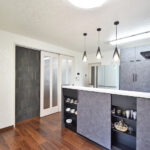 大竹市M様邸キッチンリフォーム後の施工事例写真。壁を撤去し、開放的なグレーの対面式キッチンに変更。3連ペンダントライトがおしゃれな空間。