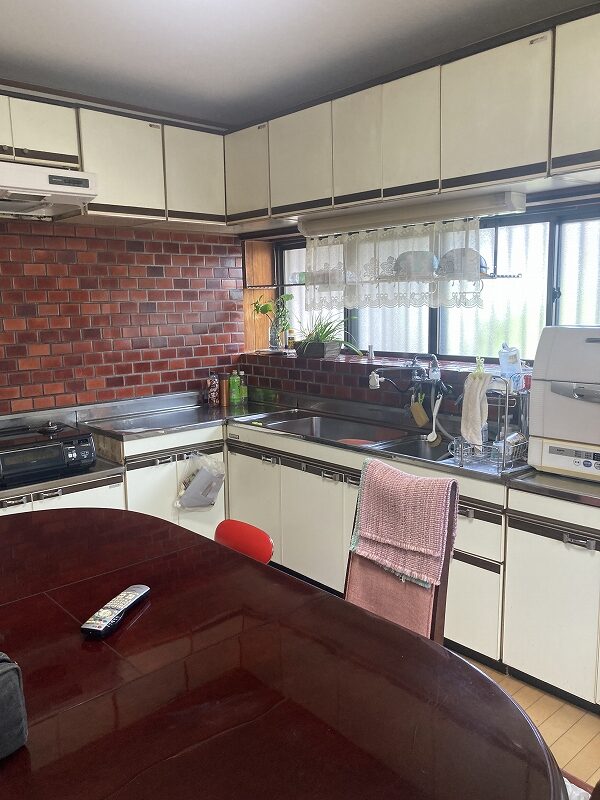 大竹市M様邸のリフォーム前施工事例画像。赤いレンガ壁が特徴的なL型キッチンで、吊戸棚によって手元が暗い状態。