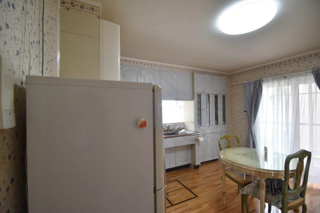 大竹市T様邸リフォーム前。壁に向かって作業するタイプのキッチン。花柄の壁紙と使い込まれた収納が特徴。