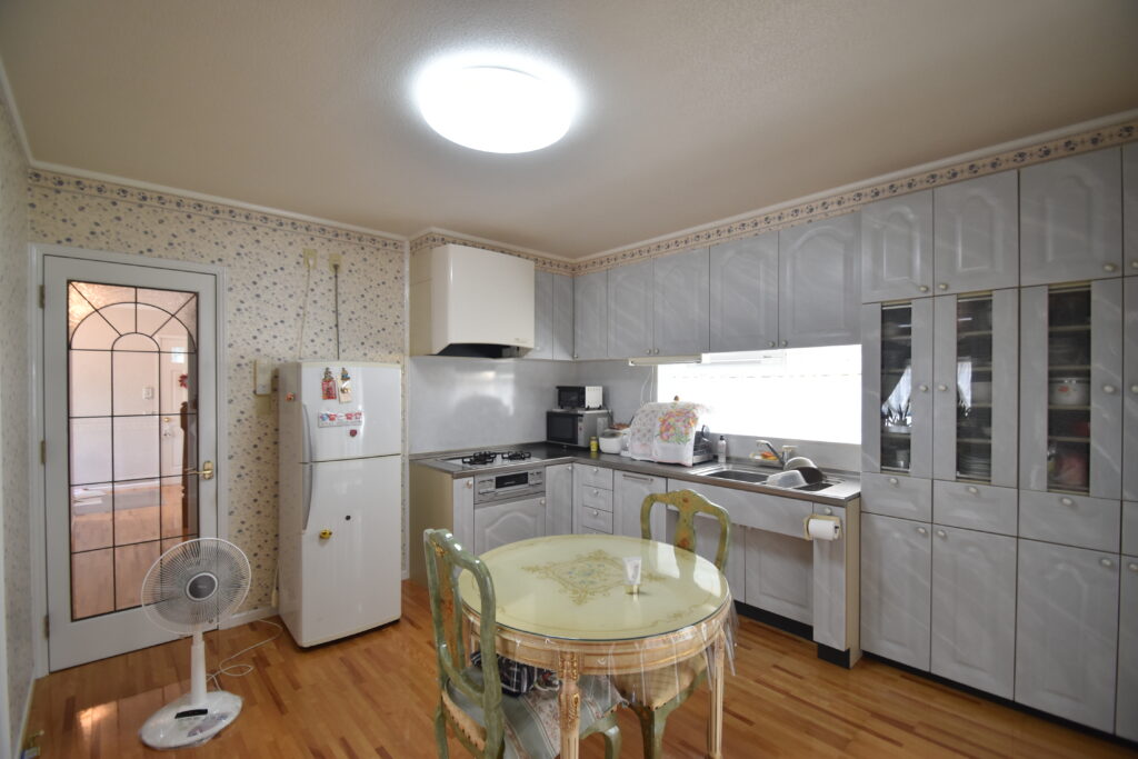 大竹市T様邸リフォーム前。壁に向かって作業するタイプのキッチン。花柄の壁紙と使い込まれた収納が特徴。