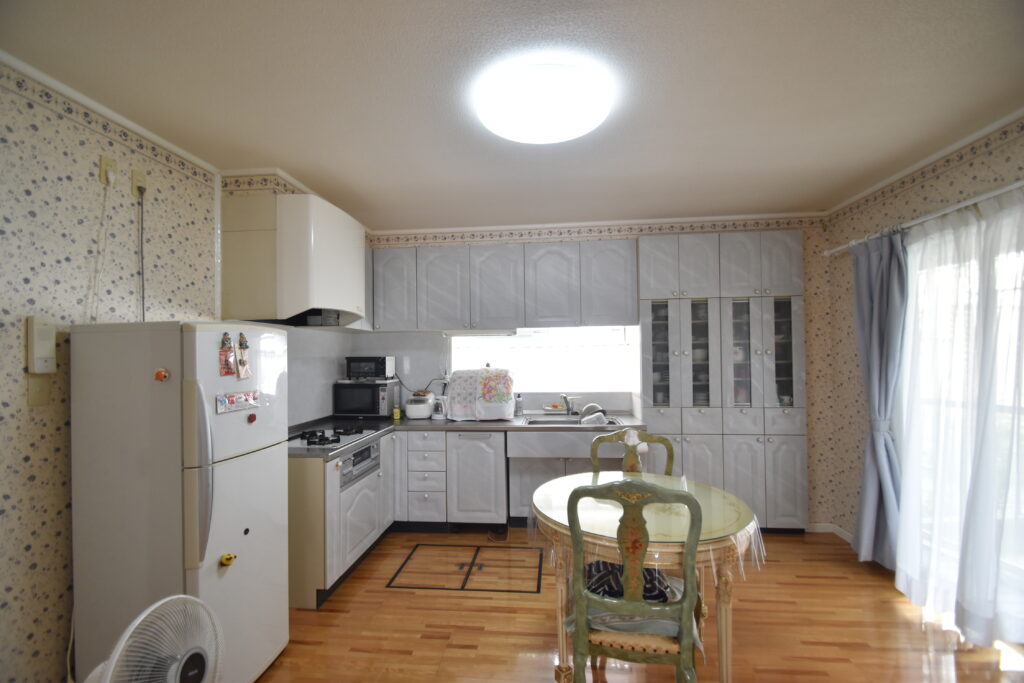 大竹市T様邸リフォーム前。壁に向かって作業するタイプのキッチン。花柄の壁紙と使い込まれた収納が特徴。